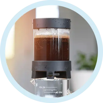 Coffee brewing device with a clear container and black base, filled with coffee.